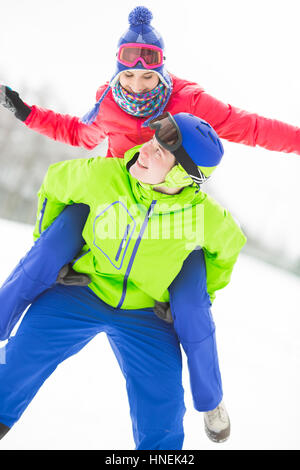 Happy young man giving piggyback ride to woman in snow Stock Photo