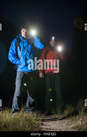 Full length portrait of male backpackers with flashlights in field at night Stock Photo