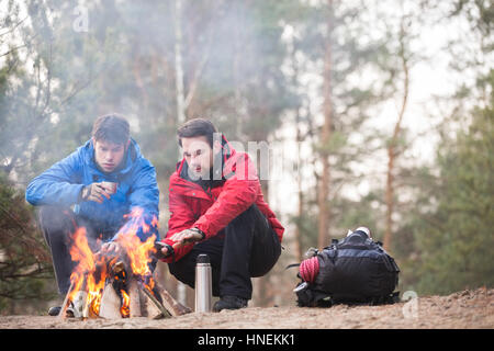 Male hikers warming hands at campfire in forest Stock Photo