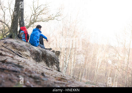 Side view of male hiker sitting on edge of cliff in forest Stock Photo