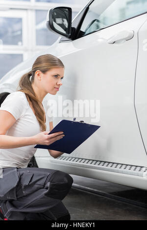 Female mechanic holding clipboard while examining car body at repair shop Stock Photo