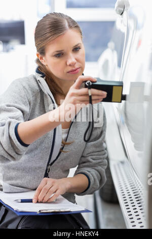 Female maintenance engineer checking car paint with equipment in workshop Stock Photo