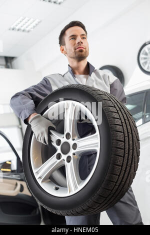 Young maintenance engineer carrying tire in automobile store Stock Photo