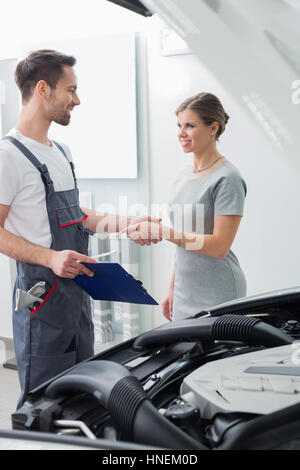 Young repair worker shaking hands with customer in car workshop Stock Photo