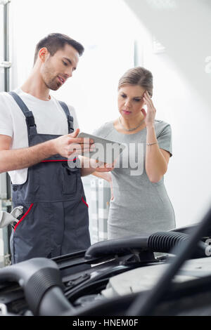 Male maintenance engineer showing digital tablet to worried customer at workshop Stock Photo