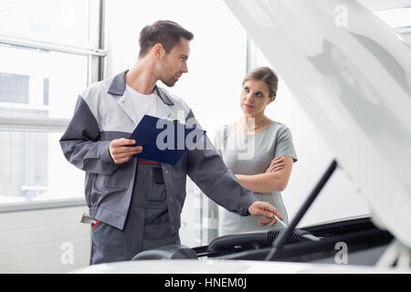 Young male engineer explaining car engine to female customer in workshop Stock Photo