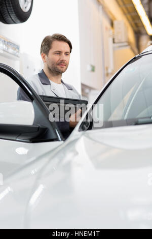 Maintenance engineer holding tablet PC while examining car in repair shop Stock Photo