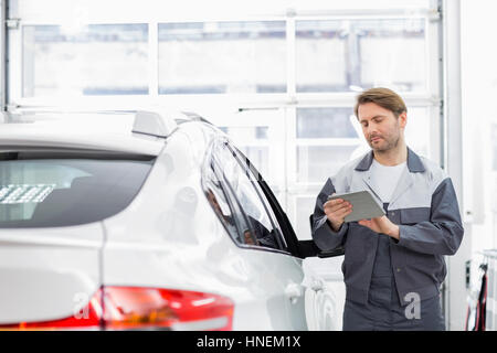 Male repair worker using tablet PC while standing by car in workshop Stock Photo