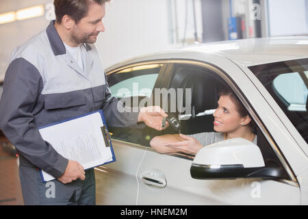 Automobile mechanic giving car key to female customer in workshop Stock Photo