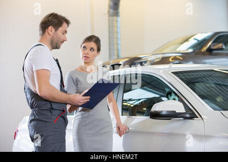 Repairman holding clipboard while conversing with female customer in automobile repair shop Stock Photo