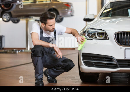 Full length of maintenance engineer cleaning car in workshop Stock Photo