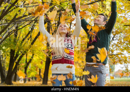 Couple enjoying falling autumn leaves in park Stock Photo