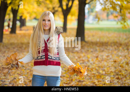 Portrait of beautiful young woman holding autumn leaves in park