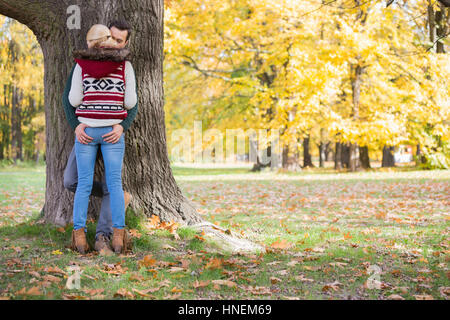 Passionate couple against tree trunk in park during autumn Stock Photo