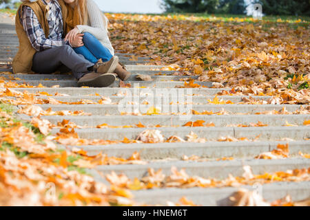 Low section of couple sitting on steps in park during autumn Stock Photo