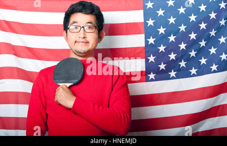 Proud Asian Man holding table tennis paddle against US Flag Stock Photo