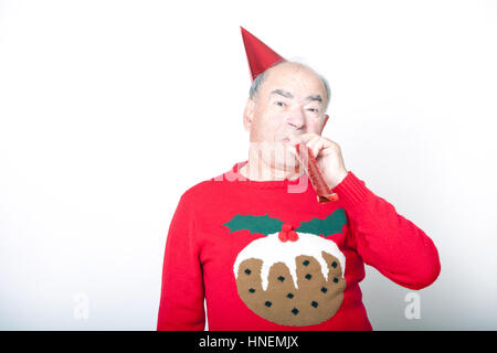 Senior adult man wearing Christmas jumper blowing party blower Stock Photo