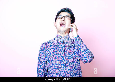 Young Geeky Asian Man in colorful shirt laughing on the phone Stock Photo