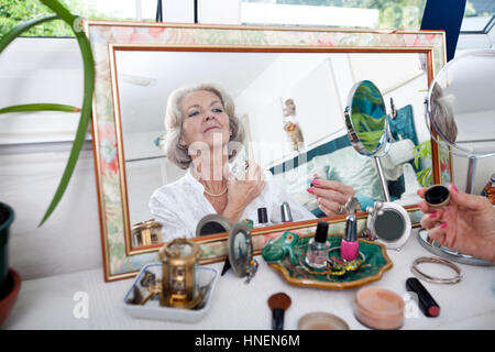 Mirror reflection of senior woman spraying perfume on herself at home Stock Photo