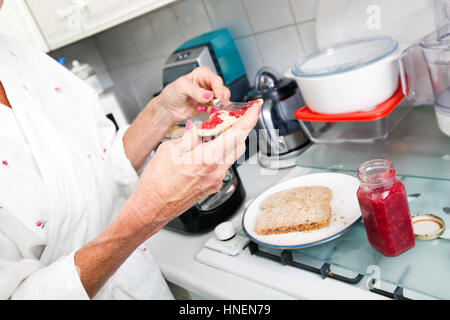 Cropped image of senior woman applying jam on toast in kitchen Stock Photo