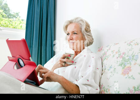 Senior woman using digital tablet while having coffee on bed at home Stock Photo