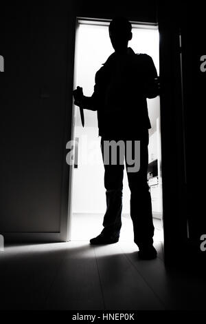 Full-length of thief with knife entering into dark room Stock Photo
