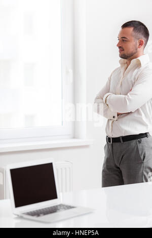 Businessman staring out of window with laptop in foreground Stock Photo
