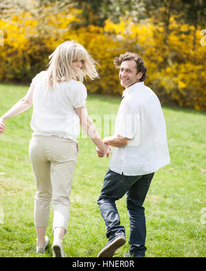 Couple holding hands with back to camera running through park Stock Photo