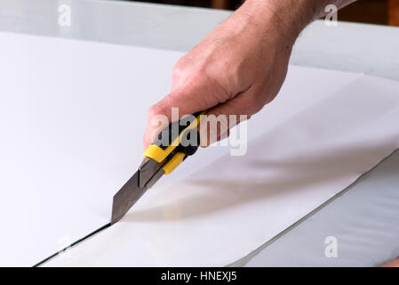 Close-up man hand with yellow utility knife cutter cutting white paper on table surface Stock Photo
