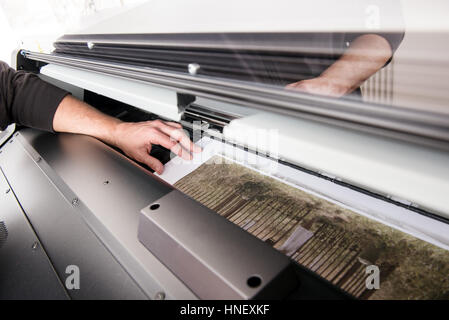 Hand of man working with wide format professional printer, while printing out graphic photo on wide paper Stock Photo
