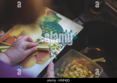 Housewife cutting fresh onion on board with kitchen sink background Stock Photo