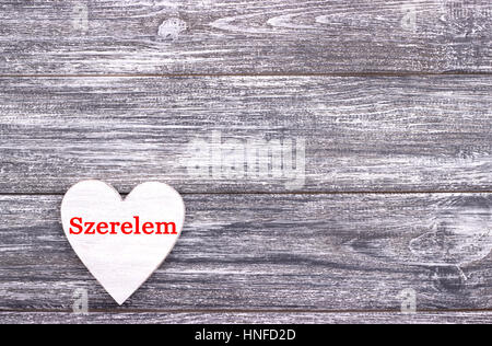 Decorative white wooden heart on grey wooden background with lettering Love in Hungurian. Valentines day card. Wedding Stock Photo