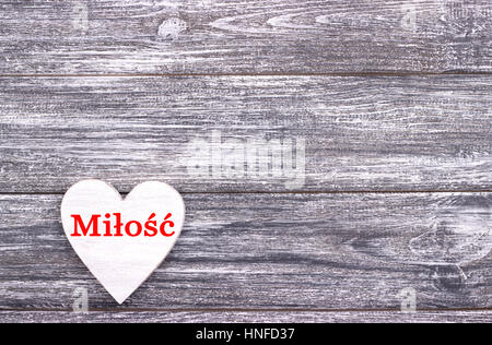 Decorative white wooden heart on grey wooden background with lettering Love in Polish. Valentines day card. Wedding Stock Photo