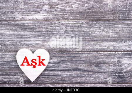 Decorative white wooden heart on grey wooden background with lettering Love in Turkish. Valentines day card. Wedding Stock Photo