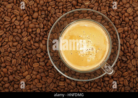 Full latte cappuccino with milk froth in big transparent glass cup with saucer on background of roasted coffee beans, elevated top view, close up Stock Photo