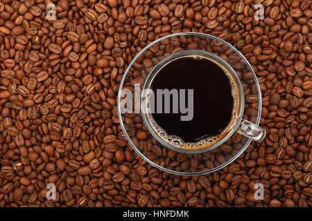 Full Americano black filtered coffee in transparent glass cup with saucer on background of roasted coffee beans, elevated top view, close up Stock Photo