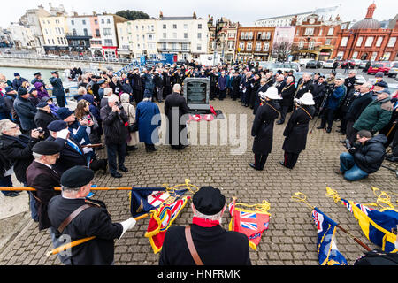 Memorial service to commemorate the 75th anniversary of Operation Fuller when the British tried to stop Germany Heavy Cruisers during the Channel Dash in world war two. People, veterans and dignitaries gathered around memorial stone during remembrance ceremony. Lowed standards in foreground. Stock Photo