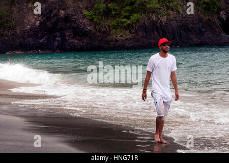 Cool Dude Strolls Along Sandy Beach in Bali Indonesia Wearing Red Baseball Hat, White T-Shirt and Short Pants Stock Photo