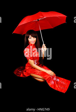 A lovely young black woman in a red Chinese dress for black background kneeling on the floor with a red umbrella in her hand.