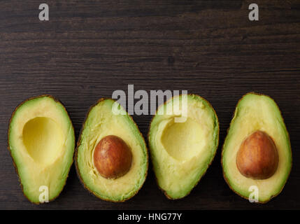 Avocado halves placed in a row on a wood surface Stock Photo