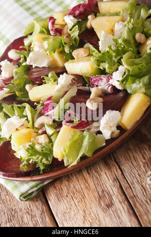 Fresh salad of beets, pineapple, goat cheese, cashews and greens mix closeup on a plate. vertical Stock Photo