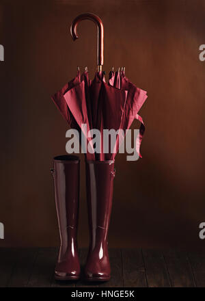 Photo in low key. Rubber boots and umbrella burgundy color on a brown background. Selective focus. Stock Photo