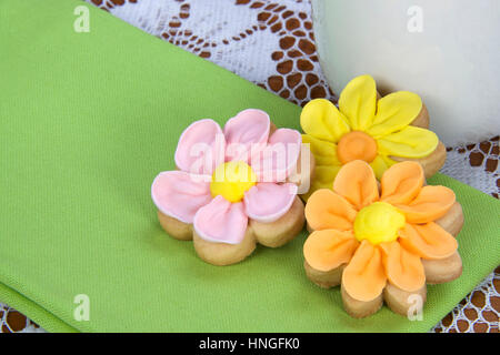 Fancy home made spring flowers sugar cookies with royal icing petals piped on. Served on a bright green napkin next to a mug of tea or coffee Stock Photo