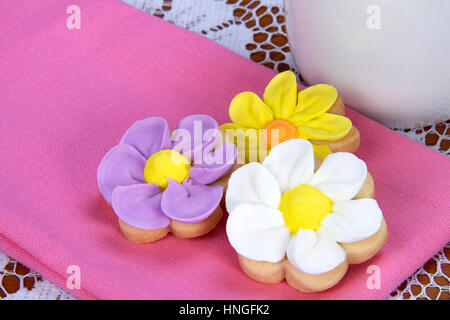 Fancy home made spring flowers sugar cookies with royal icing petals piped on. Served on a bright pink napkin next to a mug of tea or coffee Stock Photo