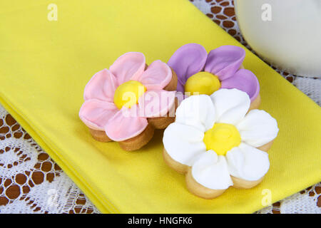 Fancy home made spring flowers sugar cookies with royal icing petals piped on. Served on a bright yellow napkin next to a mug of tea or coffee Stock Photo