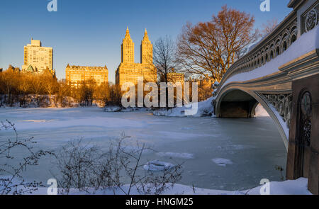 Central Park winter sunrise on the frozen Lake with the Bow Bridge and Upper West Side buildings. Wintertime in Manhattan, New York City Stock Photo