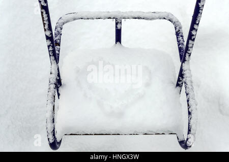 Snow-covered children's swings. On the seat in the snow figure in the shape of heart. Close up. Stock Photo