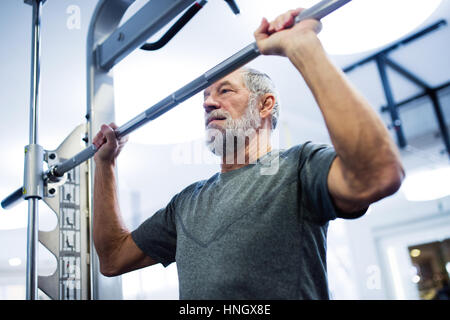 Senior man in gym doing pull-ups on horizontal bar. Stock Photo
