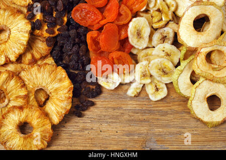 Photo of various dried fruit displayed on an old wooden table - apple rings, pineapple rings, apricots, raisins, and banana slices. Stock Photo