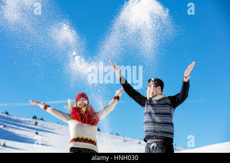 Snowball fight. Winter couple having fun playing in snow outdoors. Young joyful happy multi-racial couple. Stock Photo